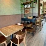 Coworking zóna RODIN – drevené stoly a regál s rastlinami pri zelenej stene